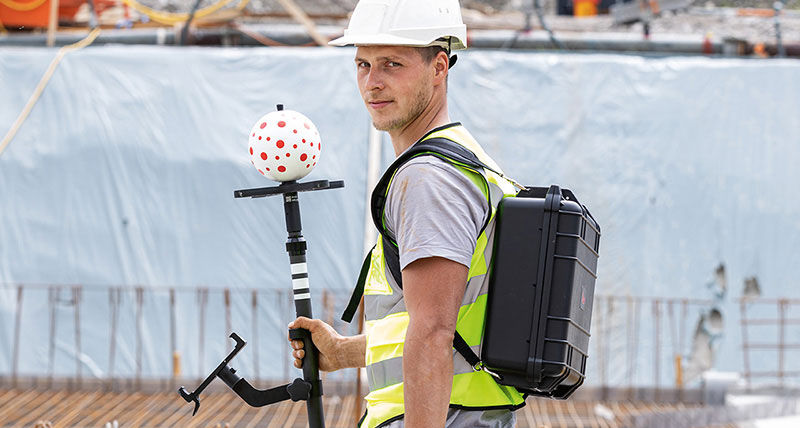 Construction worker with white hard had and Leica iCON vPole on construction site.